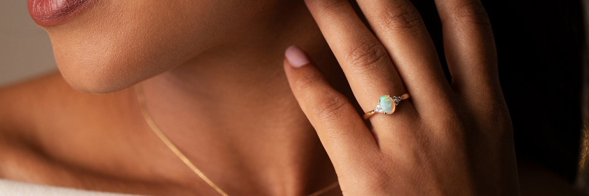 18ct yellow gold opal and diamond ring worn on a model's hand, featuring an oval opal flanked by three round brilliant cut diamonds on either side.